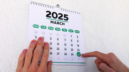Close-up of a male hand pointing finger at Eid al-Fitr date 2025 on a wall calendar