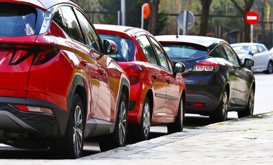 Coches rojos y negro aparcados en fila en una calle urbana de Madrid con señal de prohibido al fondo