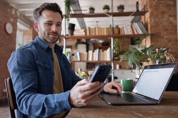 Smiling man using phone while working at desk at home