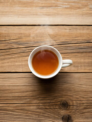 Obraz premium Hot Cup of Tea with Steam on Rustic Wooden Table Surrounded by Natural Light