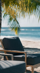 Dark gray fabric outdoor chairs with light wood frame on sandy beach, palm leaves in foreground, ocean background, suggesting relaxation and tranquility