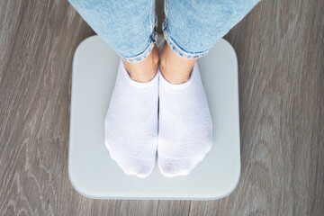 A person wearing white socks and jeans standing on a digital scale, viewed from above, symbolizing...