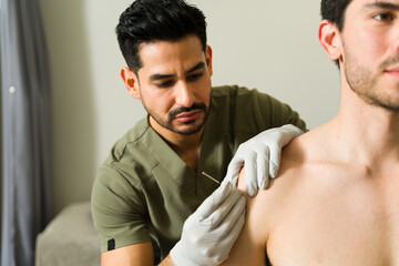 Latin physiotherapist performing dry needling technique on male patient's shoulder to alleviate...