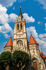 Fototapeta premium Majestic Saint Stanislaus Church with ornate tower and red-roofed turrets against a blue sky with white clouds in Chortkiv, Ternopil region, Ukraine. Gothic Revival architecture