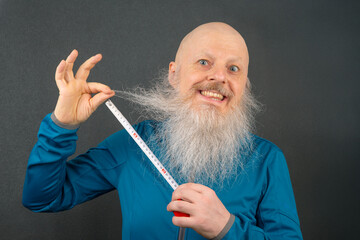 happy bald man demonstrating the length of his large white beard using a metric tape measure on a...