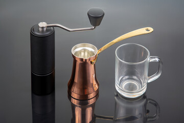 A black manual coffee grinder with a metallic handle, a copper cezve with a gold handle, and a...