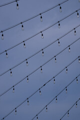 Multiple wire lines of light bulbs hanging from wires in a diagonal direction against a blue sky...
