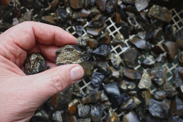 Mine, mining of tin (Sn) ore, as mineral cassiterite (SnO2). Rocks held in hand. Element used in Lithium-ion batteries, coils of superconducting magnets, pigments, solder, plating and bronze metal