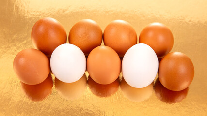 A collection of white and brown eggs on a glossy golden background, casting soft reflections in a simple yet striking food photography scene.