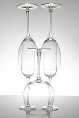 Elegant empty wine glasses with delicate stems arranged neatly, reflecting on a shiny table, set against a minimalist gray backdrop for sophisticated decor.