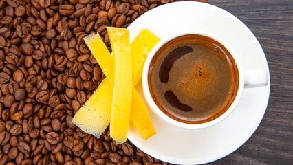 Rich espresso in a white cup paired with cheese sticks, nestled among coffee beans on a rustic wooden surface, perfect for a gourmet breakfast.