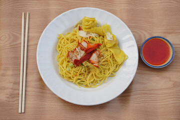 Yellow noodle on white plate, chopsticks and red sauce, placed on wooden background. Concept, traditional food. Delicious menu. Healthy eating. Top view. 