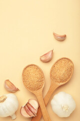 Fresh garlic and garlic powder on spoon on beige background. Using spices for meals. Top view