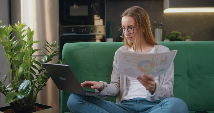 Woman working with laptop and documents collating data and checking reports of employees. Modern business freelancer female paperwork use laptop working remotely at home.