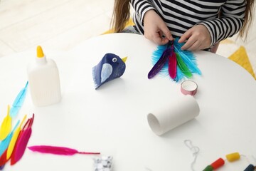 Little girl making paper bird at white table indoors, closeup. Child handmade craft