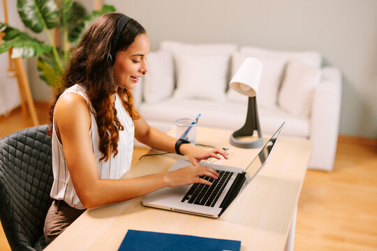 Smiling businesswoman working from home using headset and typing on a laptop
