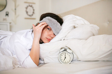 A cozy bedroom scene: a woman in a sleep mask, next to an alarm clock and a cup of tea, enjoying a slow morning.