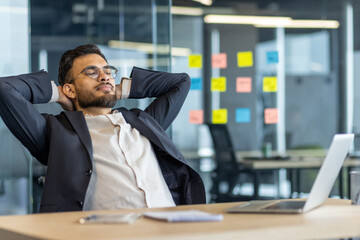 Businessman relaxing and resting inside the office. Man in business suit with hands behind head...
