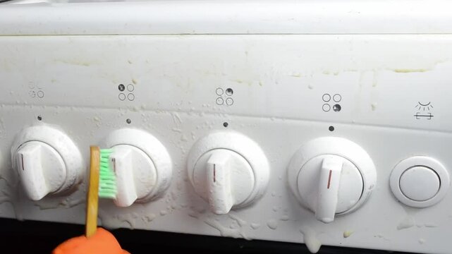 Person is brushing the knobs of a stove. The knobs are dirty and the person is trying to clean them