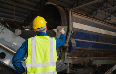 A waste management engineer monitors a large industrial waste separator at a recycling facility,...