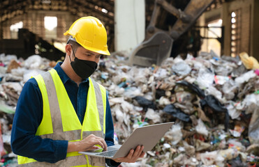 An environmental engineer in safety gear works on a laptop at a recycling facility, managing waste...