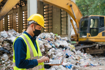 A recycling engineer wearing protective gear analyzes waste data on a laptop at a landfill site, ensuring efficient waste management practices.