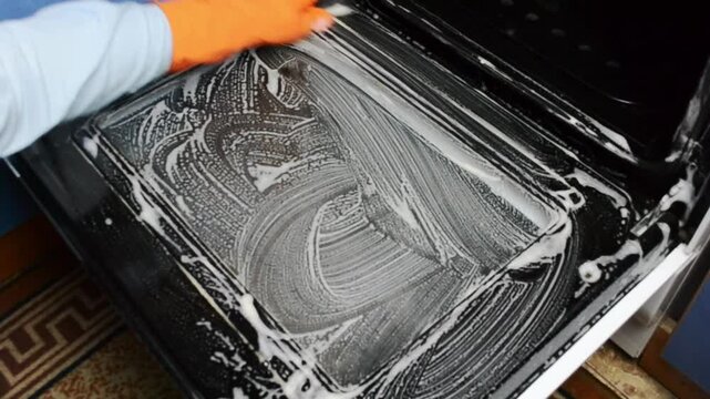 Person is cleaning a dirty oven with a brush and a sponge. The oven is covered in grease and grime, and the person is scrubbing it vigorously to remove the dirt. Concept of hard work