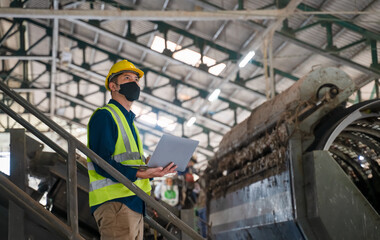 A recycling engineer inspects a waste sorting machine inside a recycling plant, ensuring compliance...
