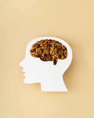 Walnuts visible through a head profile with brain paper cutout on beige background. Creative healthy food for brain concept. Flat lay style. Top view banner.