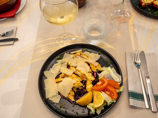 Delicious chicken salad with parmesan cheese, tomatoes and lemon slices served on black plate in elegant restaurant