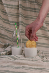 milk in a transparent bottle. a straw sticks out of the bottle, and next to it is a round cookie. a person's hand dips a cookie into a transparent glass
