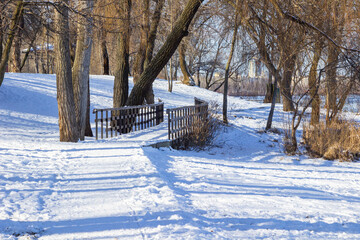Snow lies on the ground. Shadows on the snow. Wooden bridge across frozen river.