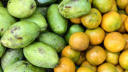 Fresh green mangoes and ripe oranges create vibrant display of colors and textures, showcasing nature bounty in market setting