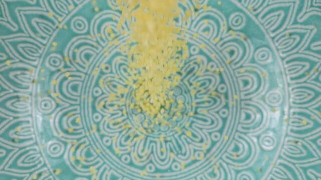 Couscous grits are poured into a blue ceramic bowl. Top view. Slow motion.