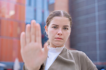 Serious young woman raising her hand in a stop gesture, expressing determination and...