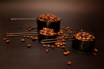 coffee beans roasted in measuring cups on a dark background scattered