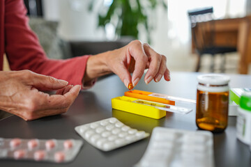 Senior woman organizing medications at home, carefully placing pills into a weekly pill organizer....