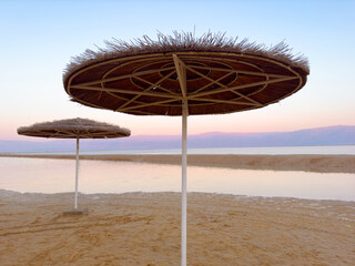 Parasol straw umbrella near sea shore. Straw umbrellas on hot summer day by beach. Sunny blue skies warm weather enjoyed on beach under parasol made of straw. Vacation in tropical countries