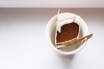 Drip bag in a ceramic cup on windowsill. Instant freshly brewed alternative filter drink in mug. Easy brew black coffee method for home, travel or office. cozy trendy lifestyle