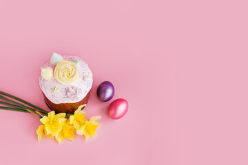 Traditional russian Easter ortodox cake with daffodil flower and colorful eggs on light pink background. Kulic, Kulich, Paska homemade bread with glaze. Spring christian holiday. Festive celebration