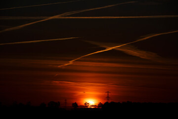 Sunset over the horizon casting vibrant colors across the sky with silhouettes of trees and power...