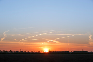 Fototapeta premium Beautiful sunset over a tranquil landscape with crisscrossing clouds painted across the sky at dusk