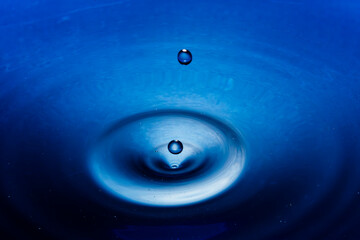 Water droplet splashing into deep blue liquid creating ripples and concentric circles in a tranquil setting