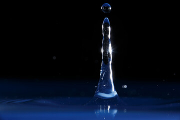 Water droplet creates a stunning splash in dark background with illuminated reflections