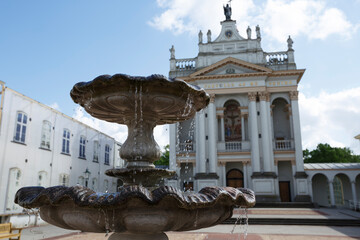 Historic fountain in front of a grand church in bright sunlight during midday in a serene courtyard...
