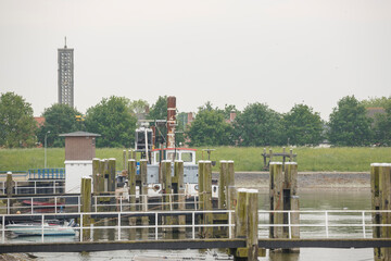 Obraz premium Boats docked at a quiet harbor with a distant tower on an overcast day in a small coastal town