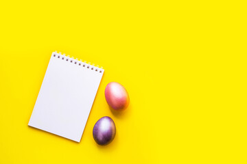 Flat lay with notebook mock up and colorful painted eggs on yellow background. Spring note trendy minimal holiday concept, place for text, logo, wishes. Empty space, list, mockup. Top view