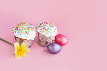 Traditional russian Easter ortodox cake with daffodil flower and colorful eggs on light pink background. Kulic, Kulich, Paska homemade bread with glaze. Spring christian holiday. Festive celebration