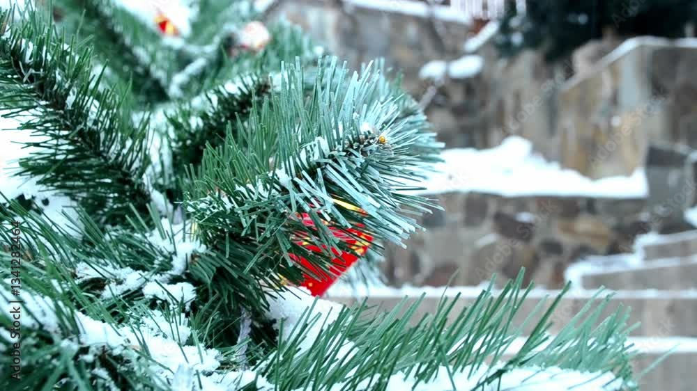 Poster christmas tree with snow on it and a red ornament hanging from it. the tree is surrounded by a stone
