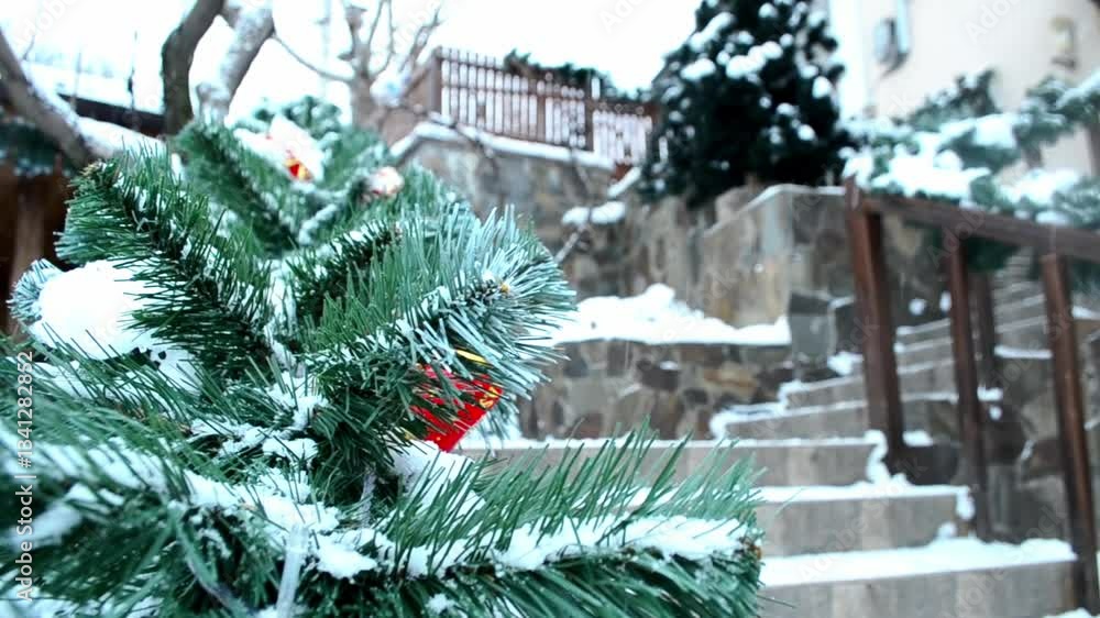 Poster snow covered tree with a red ornament on it. the tree is surrounded by a stone wall and steps